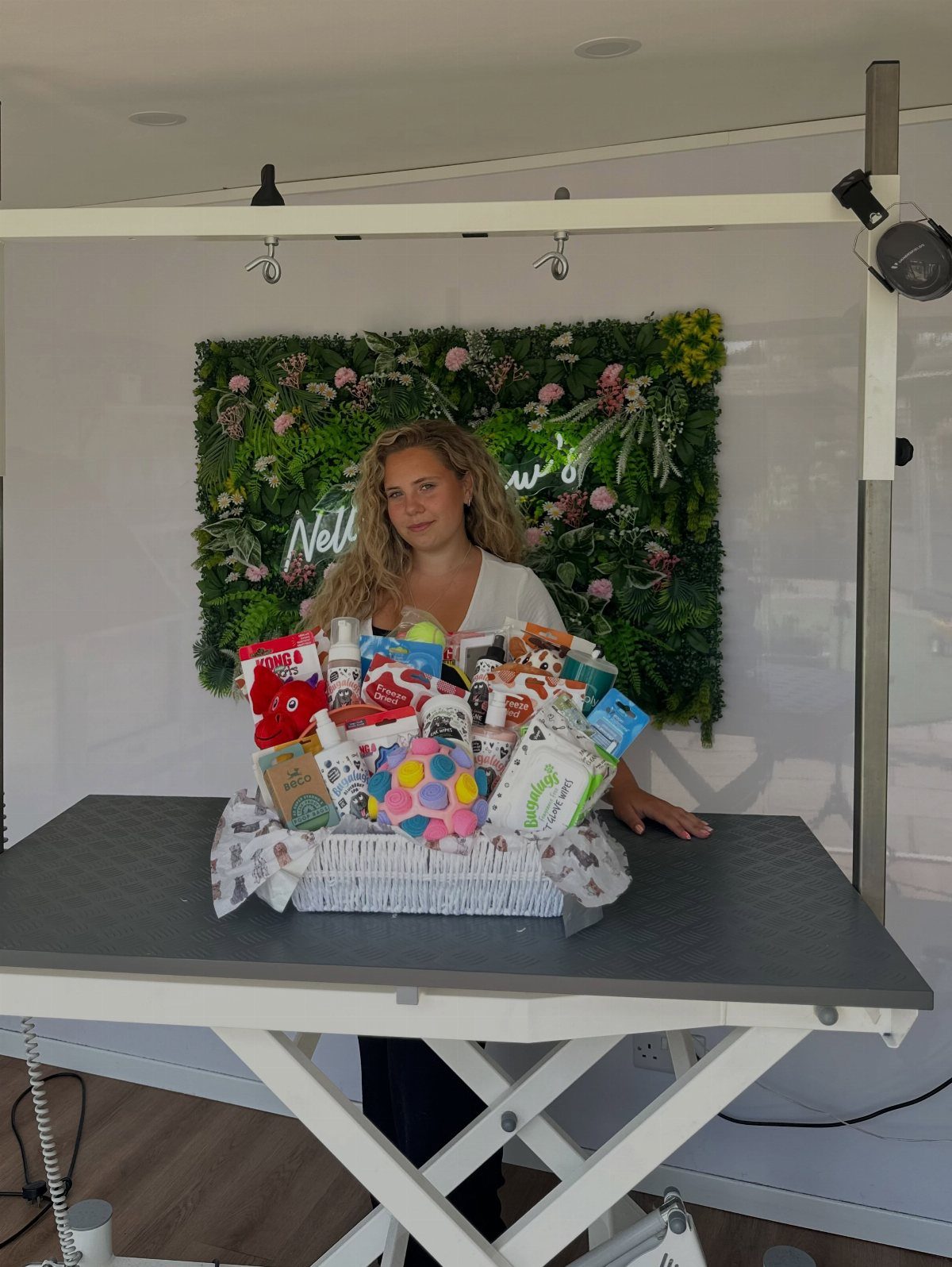 Woman presenting a white gift basket filled with colorful pet toys and supplies.