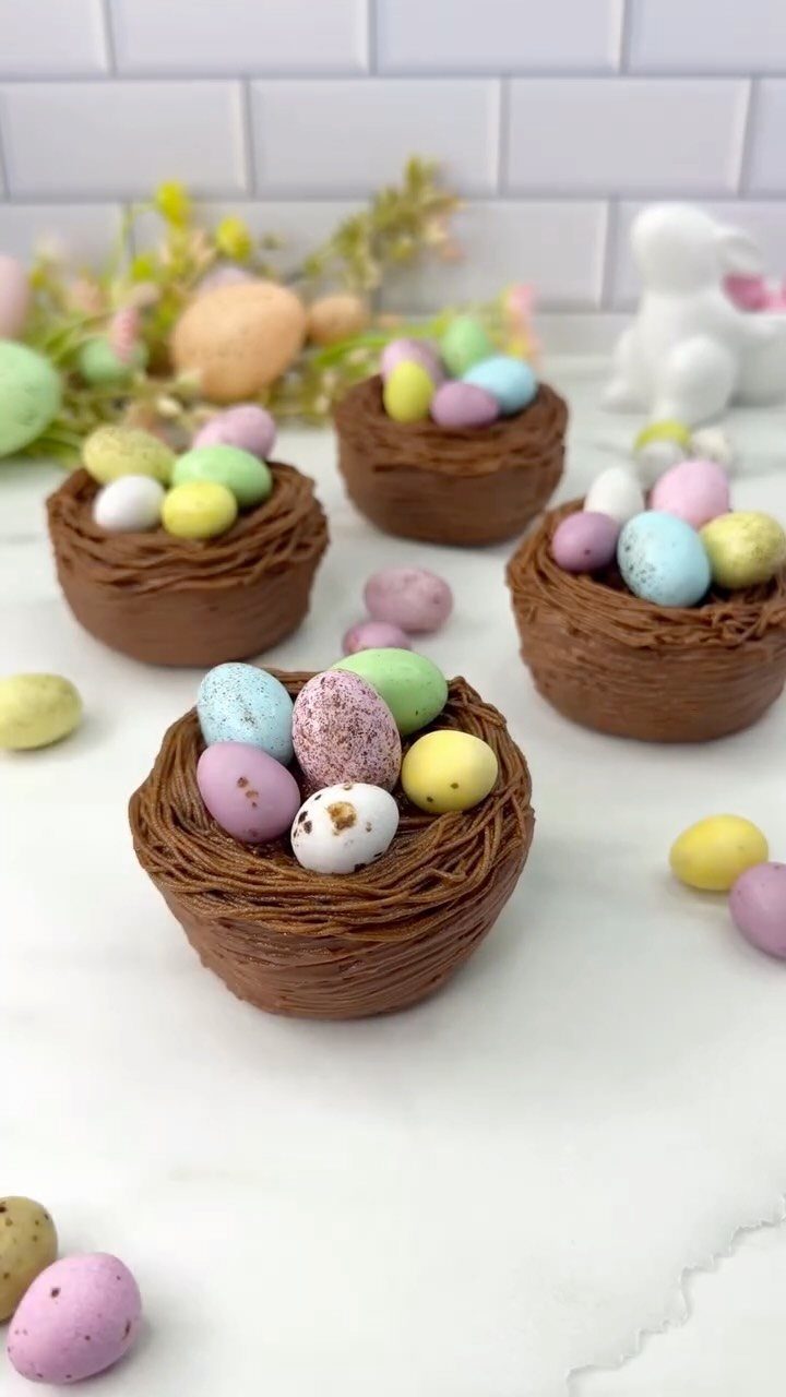 Chocolate nests filled with colorful candy eggs on a white surface with spring decor
