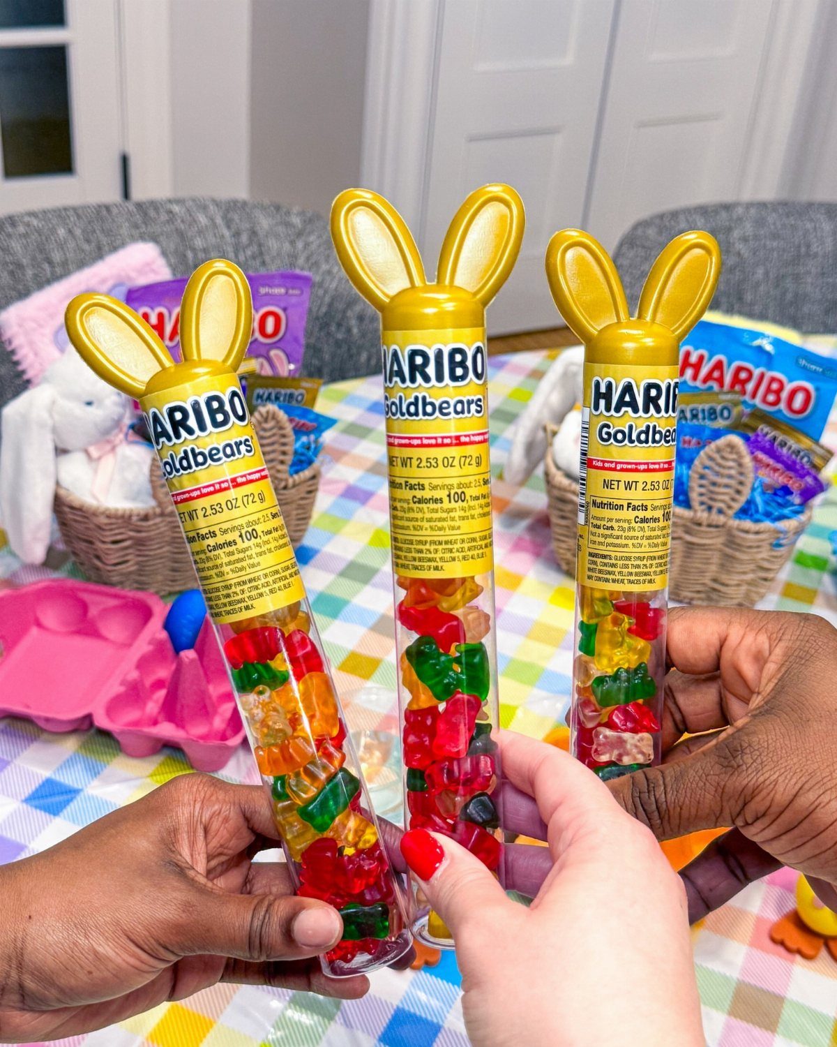 Three people holding Haribo gummy bear tubes with yellow bunny ear caps.