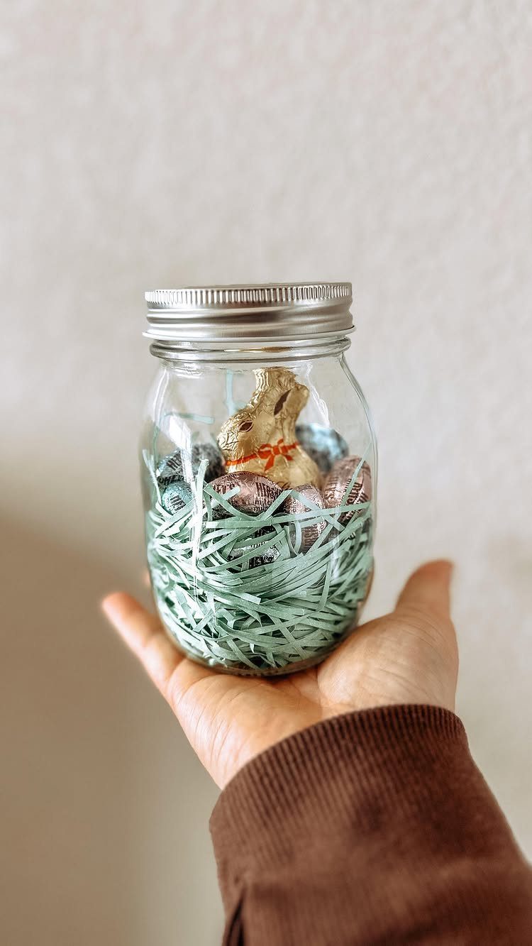 Mason jar filled with blue shredded paper, chocolate eggs, and a bunny figurine.