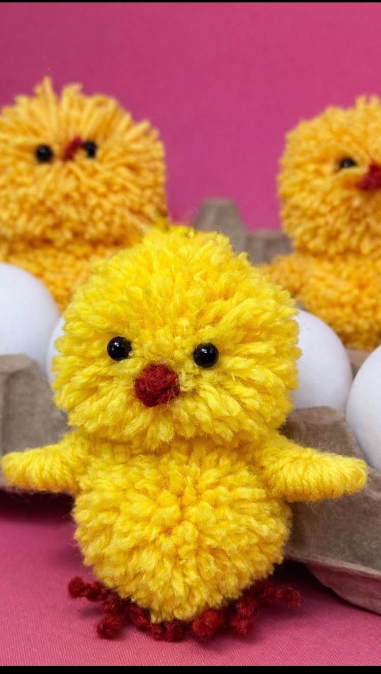 Yellow fuzzy yarn chicks sitting in a cardboard egg carton with white eggs.