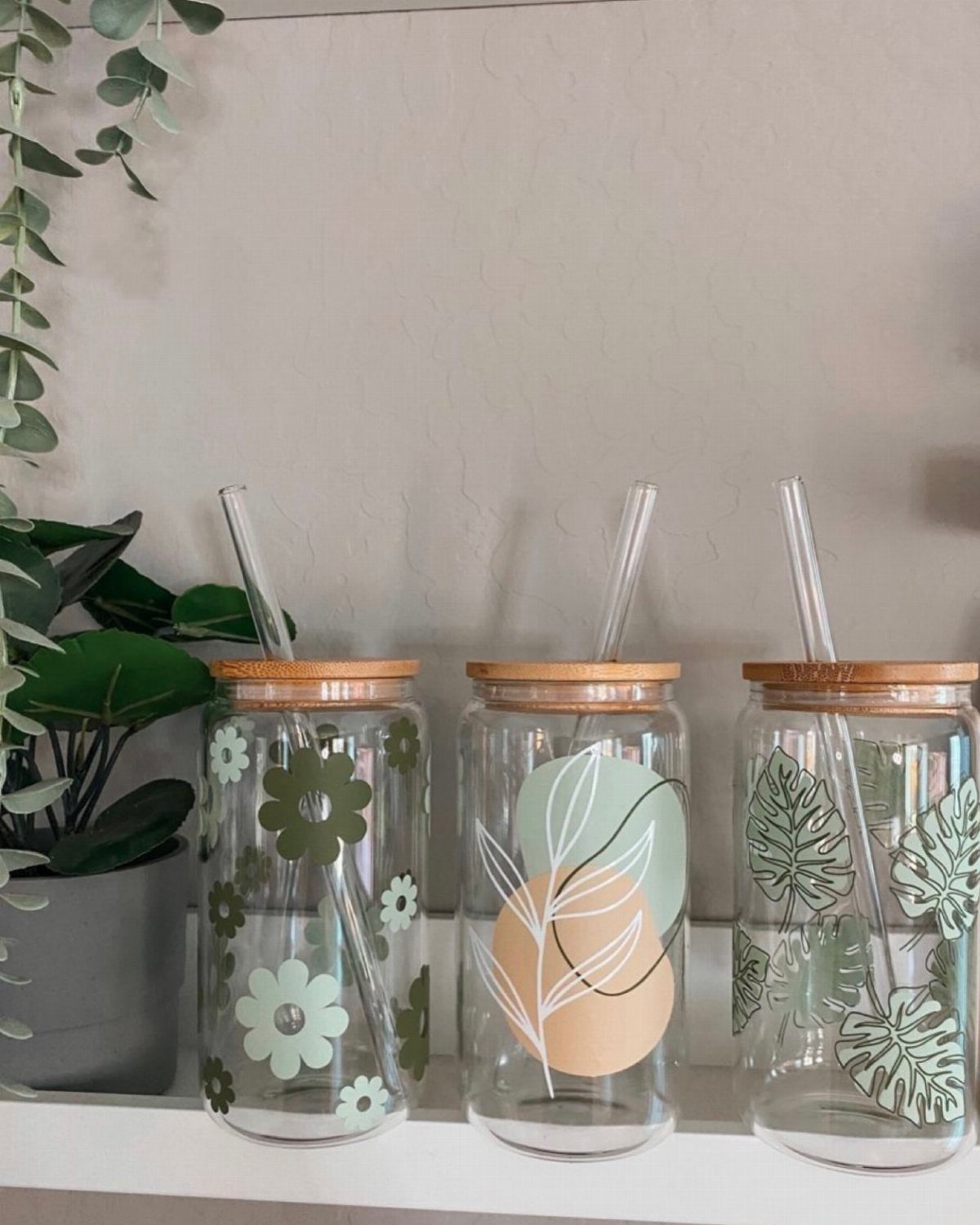 14 Small Unisex Gifts for Friends, Coworkers and Family 6 Three glass jars with bamboo lids and botanical designs on a white shelf.