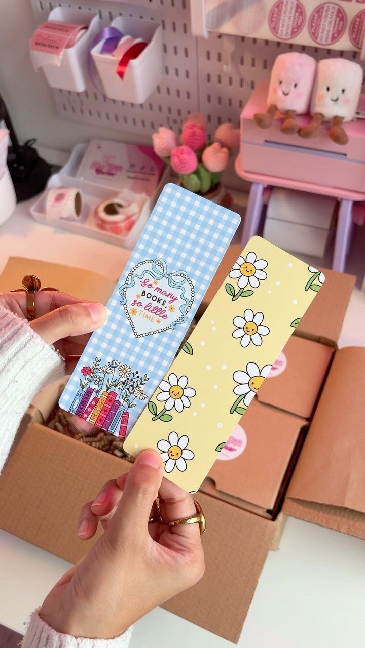 14 Small Unisex Gifts for Friends, Coworkers and Family 3 Two decorative bookmarks, one blue and one yellow, held over a shipping box.