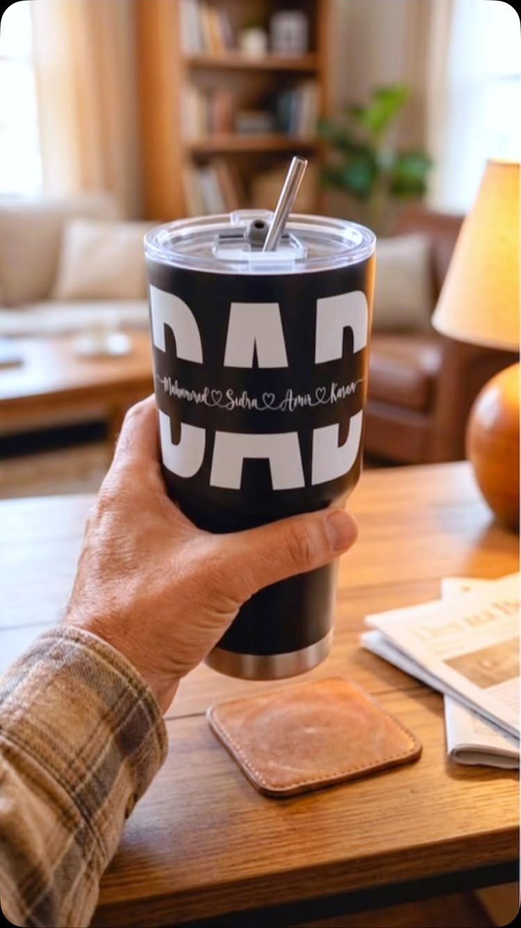 11 Step Father Gifts: From a Pocket Knife to a Photo Plaque 9 Black insulated tumbler with DAD text held by a hand over wooden table
