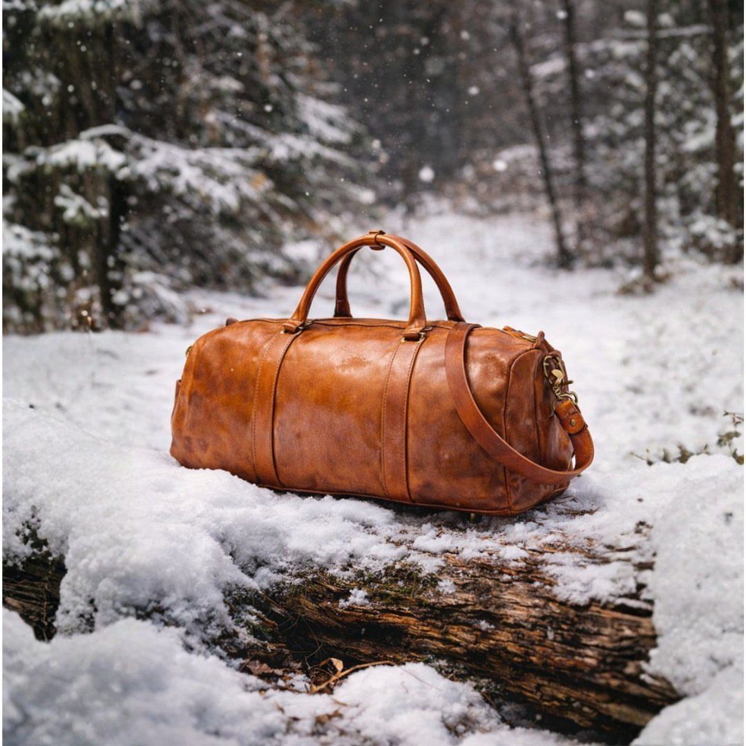 11 Step Father Gifts: From a Pocket Knife to a Photo Plaque 2 Brown leather travel duffel bag sitting on a snow-covered log in a winter forest.