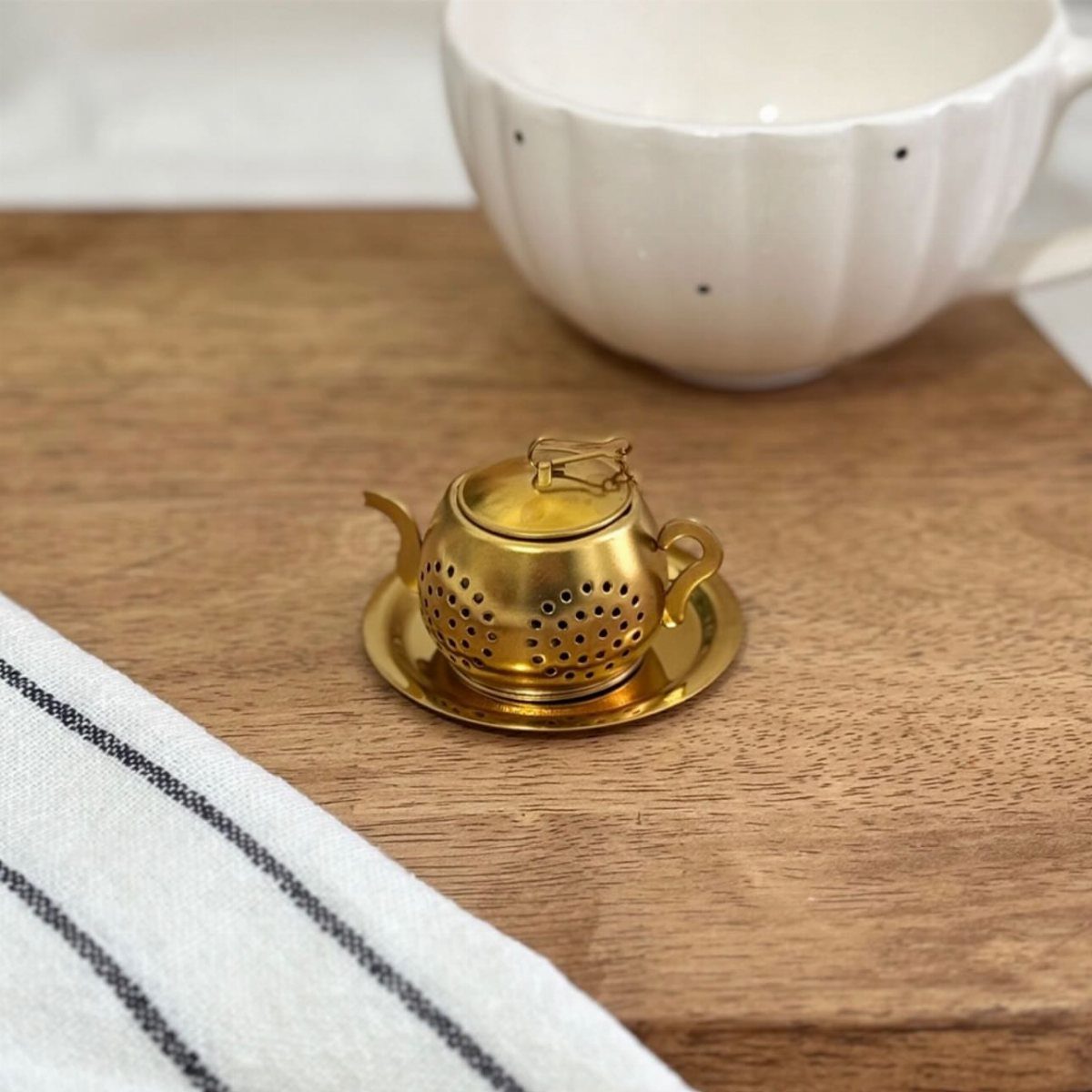 Tea Bag Gift Ideas to Make or Buy: 11 Sweet Picks 10 Gold teapot-shaped tea infuser on a wooden board next to a white cup.