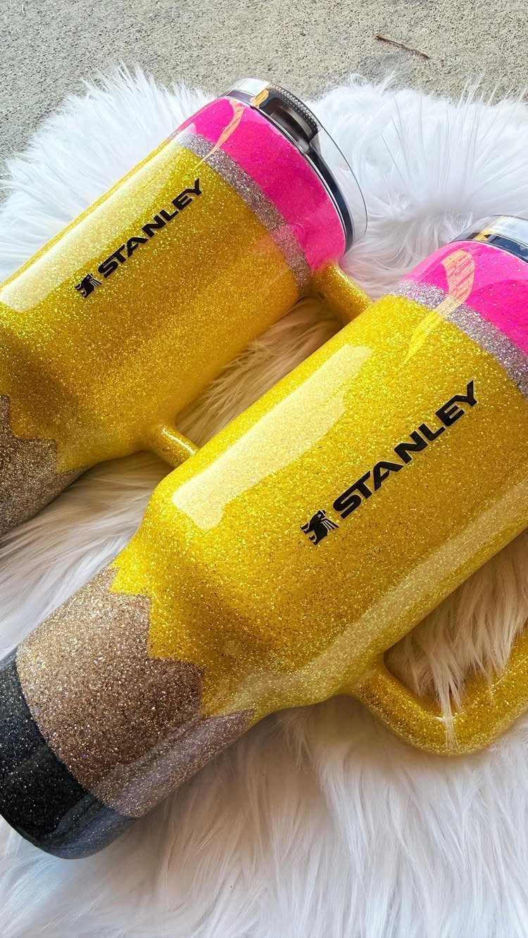 Two yellow glittery Stanley tumblers designed as pencils on white faux fur.