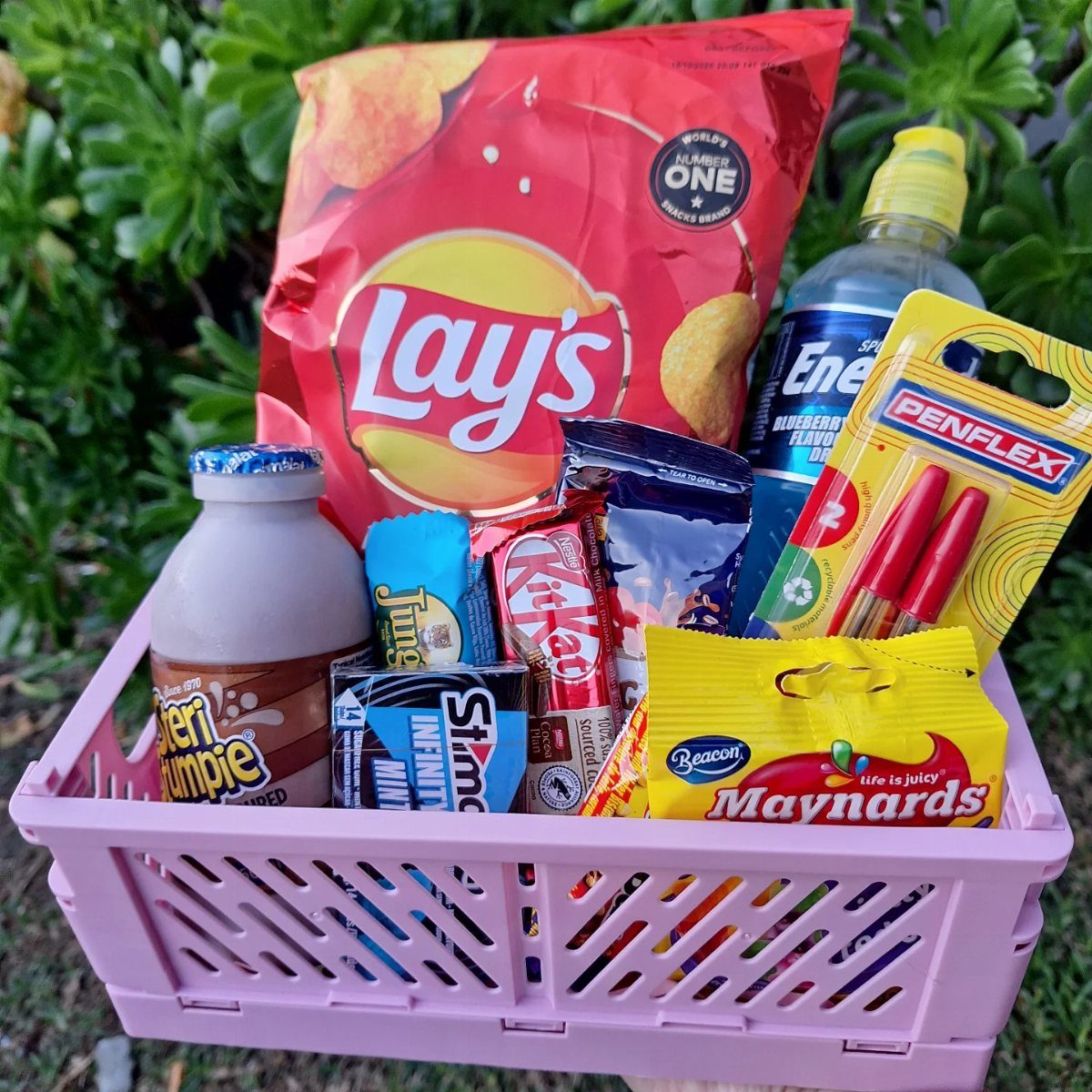 Pink basket filled with Lay's chips, chocolate milk, candy, and red pens.
