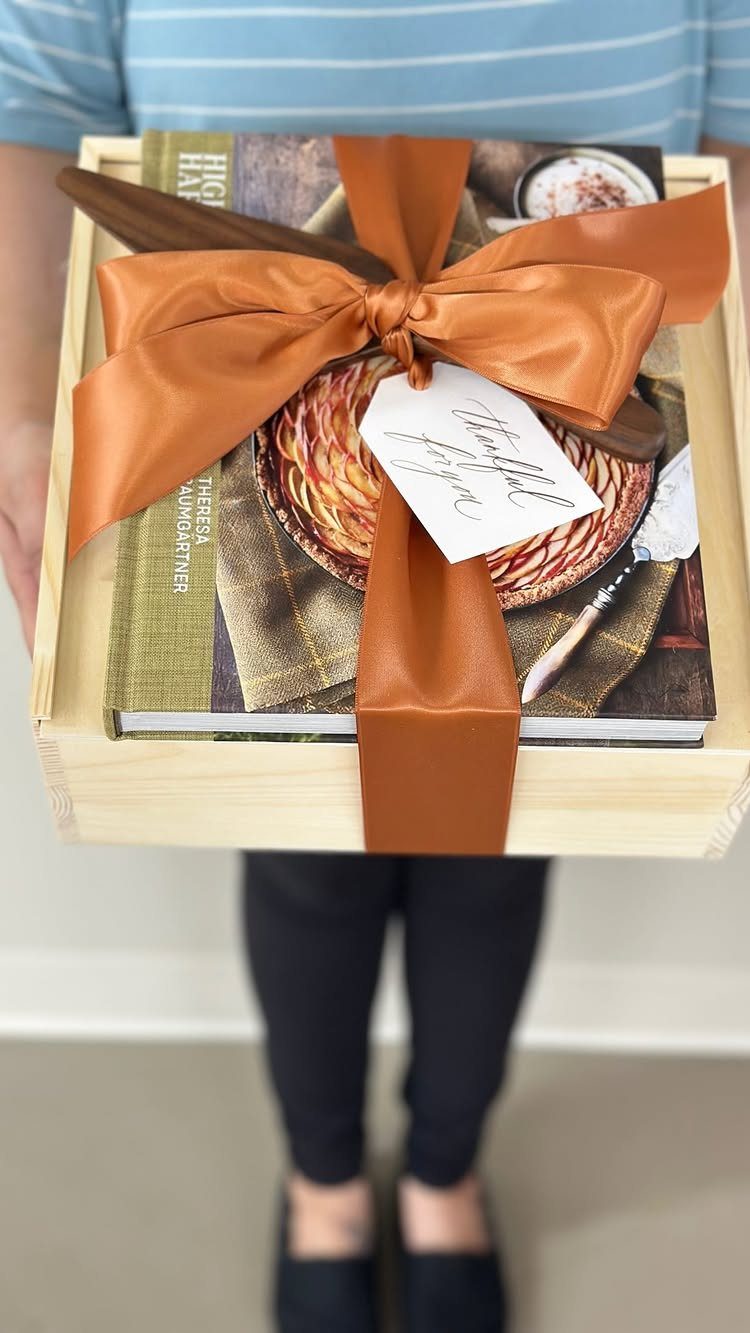 8 Thanksgiving Gift Box Ideas for Hosts and Friends 8 Wooden gift box with a cookbook and orange ribbon held by a person