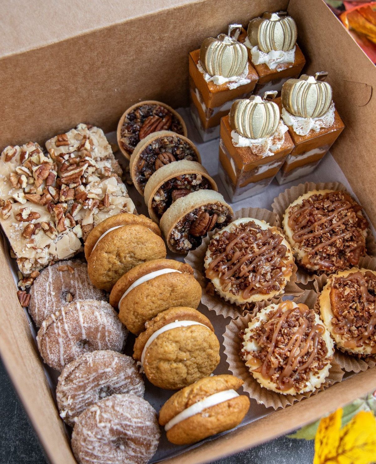 8 Thanksgiving Gift Box Ideas for Hosts and Friends 2 Assorted desserts in a cardboard box featuring gold pumpkin cake toppers and pecan treats.