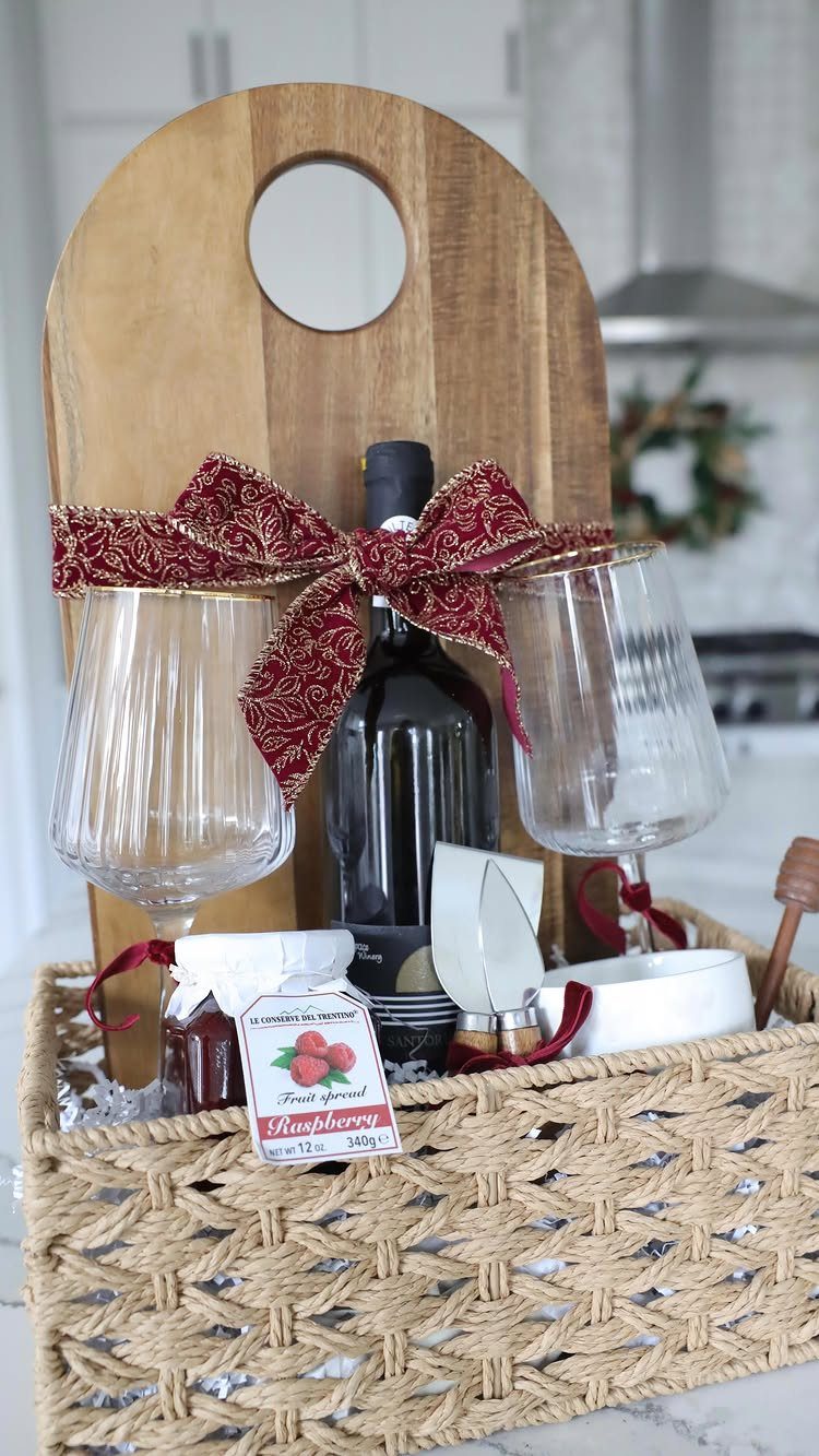 8 Thanksgiving Gift Box Ideas for Hosts and Friends 5 Woven gift basket with wine, glasses, wooden board, and jam tied with red bow.