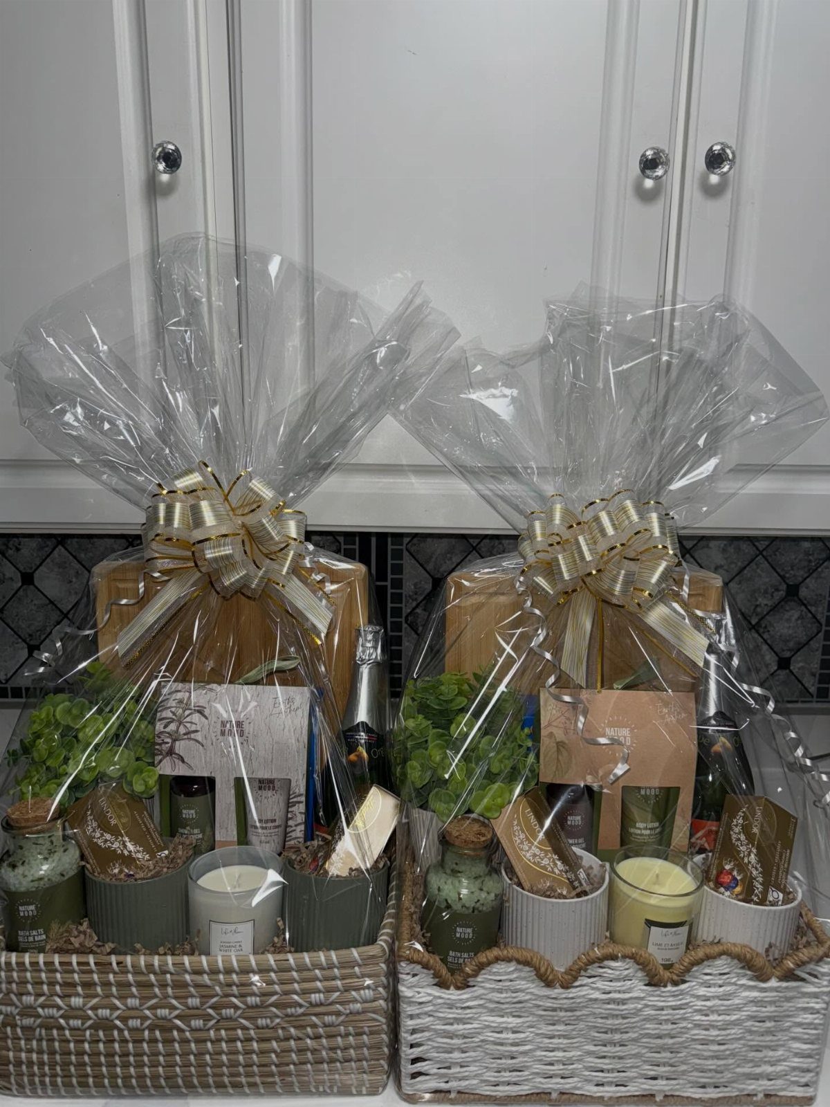 11 Thanksgiving Gifts for Family, From Candles to Cozy Throws 1 Two wrapped gift baskets containing wooden boards, candles, and plants in a kitchen.