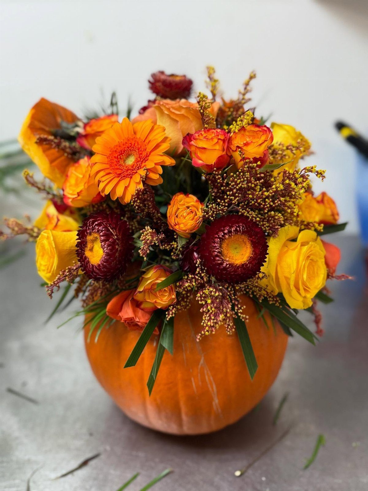 11 Thanksgiving Gifts for Family, From Candles to Cozy Throws 4 Autumn floral arrangement with orange and yellow flowers inside a carved pumpkin