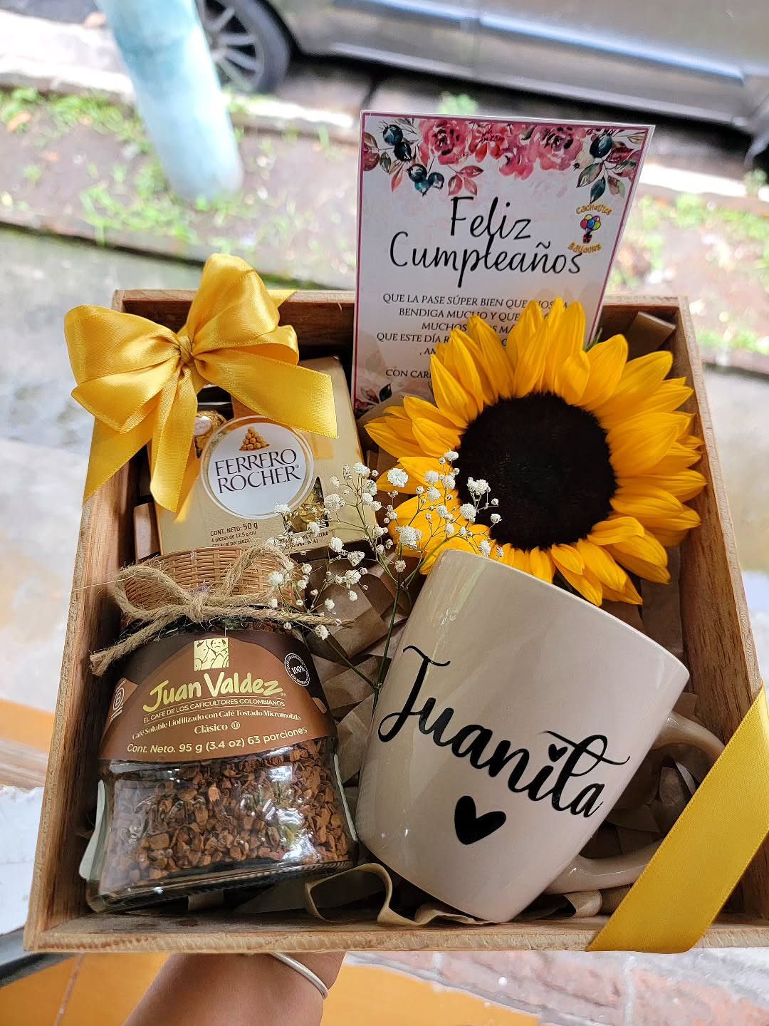 Wooden gift basket with coffee, a personalized mug, chocolates, and a sunflower.