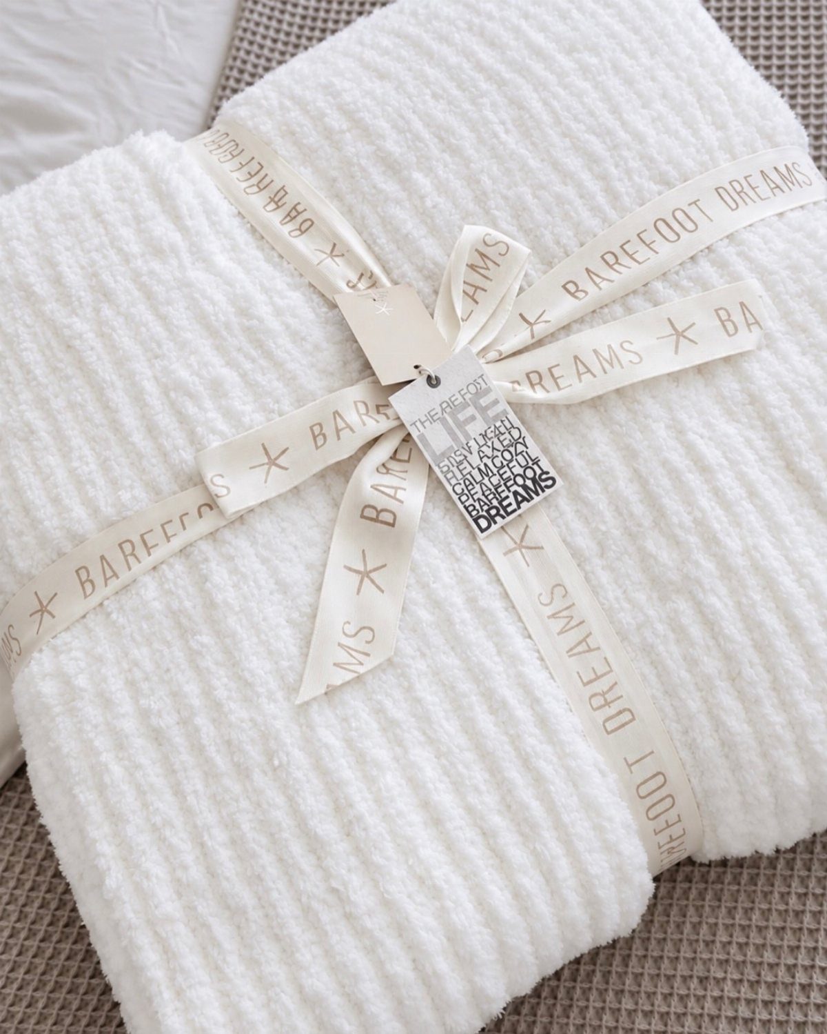 29 Trendy Gift Ideas for Her: The 2026 Gift Guide 5 White Barefoot Dreams plush blanket tied with a branded ribbon and gift tag.