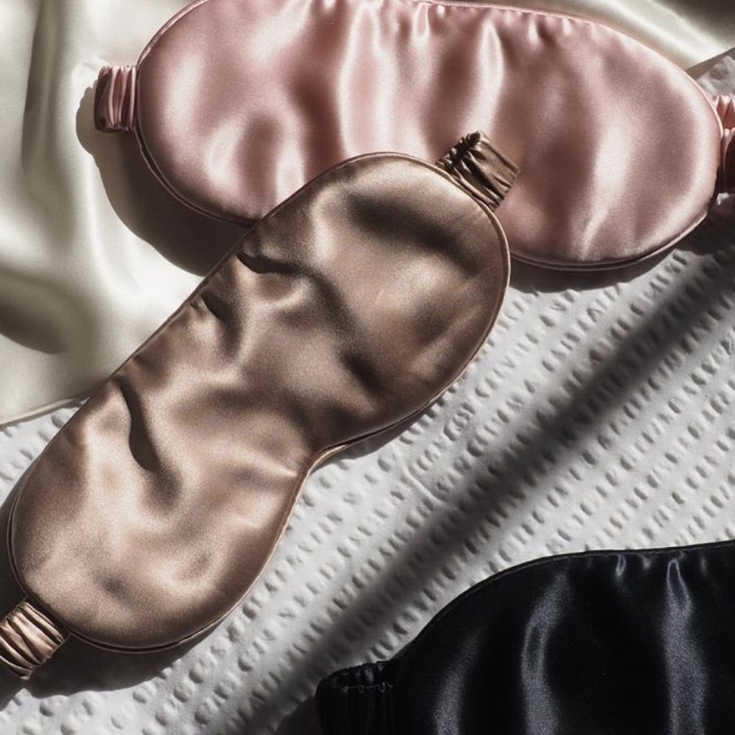 29 Trendy Gift Ideas for Her: The 2026 Gift Guide 17 Satin sleep masks in pink, champagne, and black on white textured fabric.