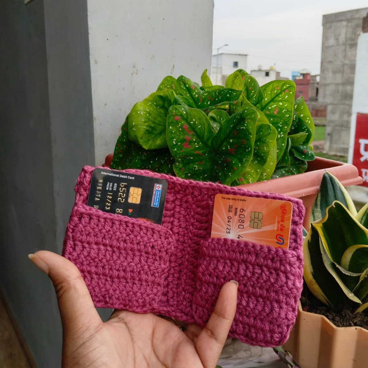 Pink crocheted wallet holding two bank cards held in a person's hand.