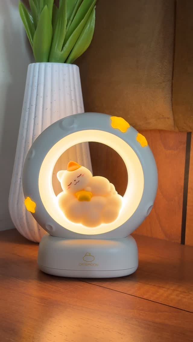 Circular grey night light with a glowing cat on a cloud on wood