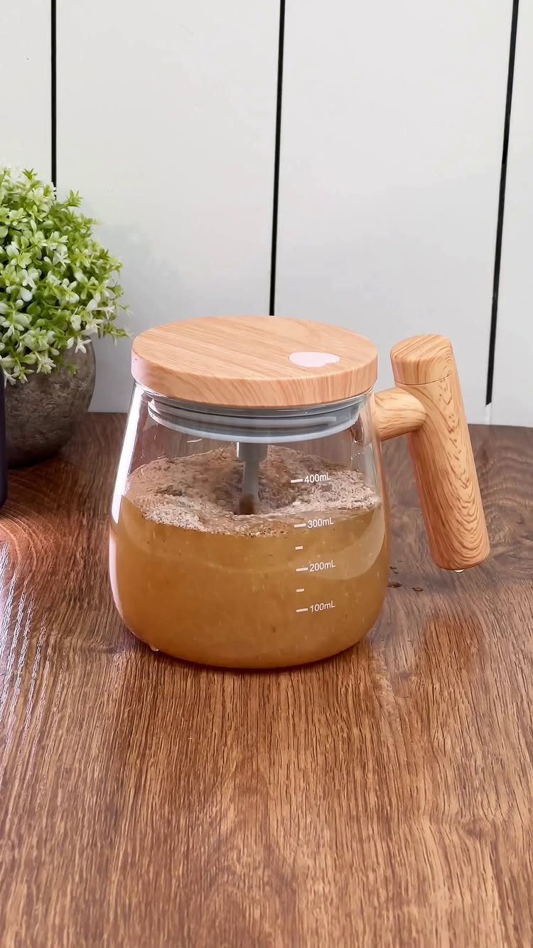 Glass teapot with wooden lid and handle filled with tea on wooden table