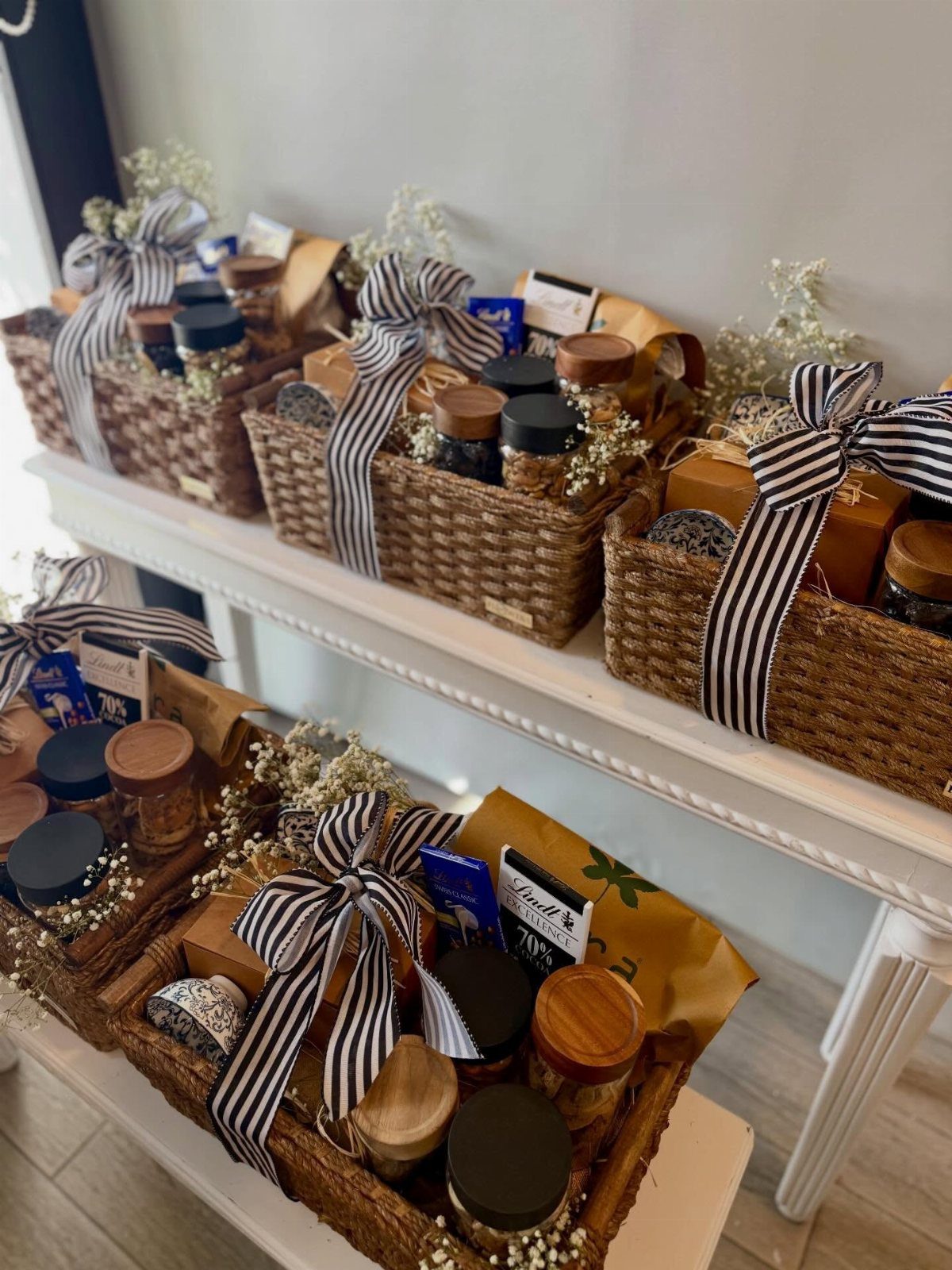 Woven wicker gift baskets filled with gourmet jars and snacks with striped ribbons.