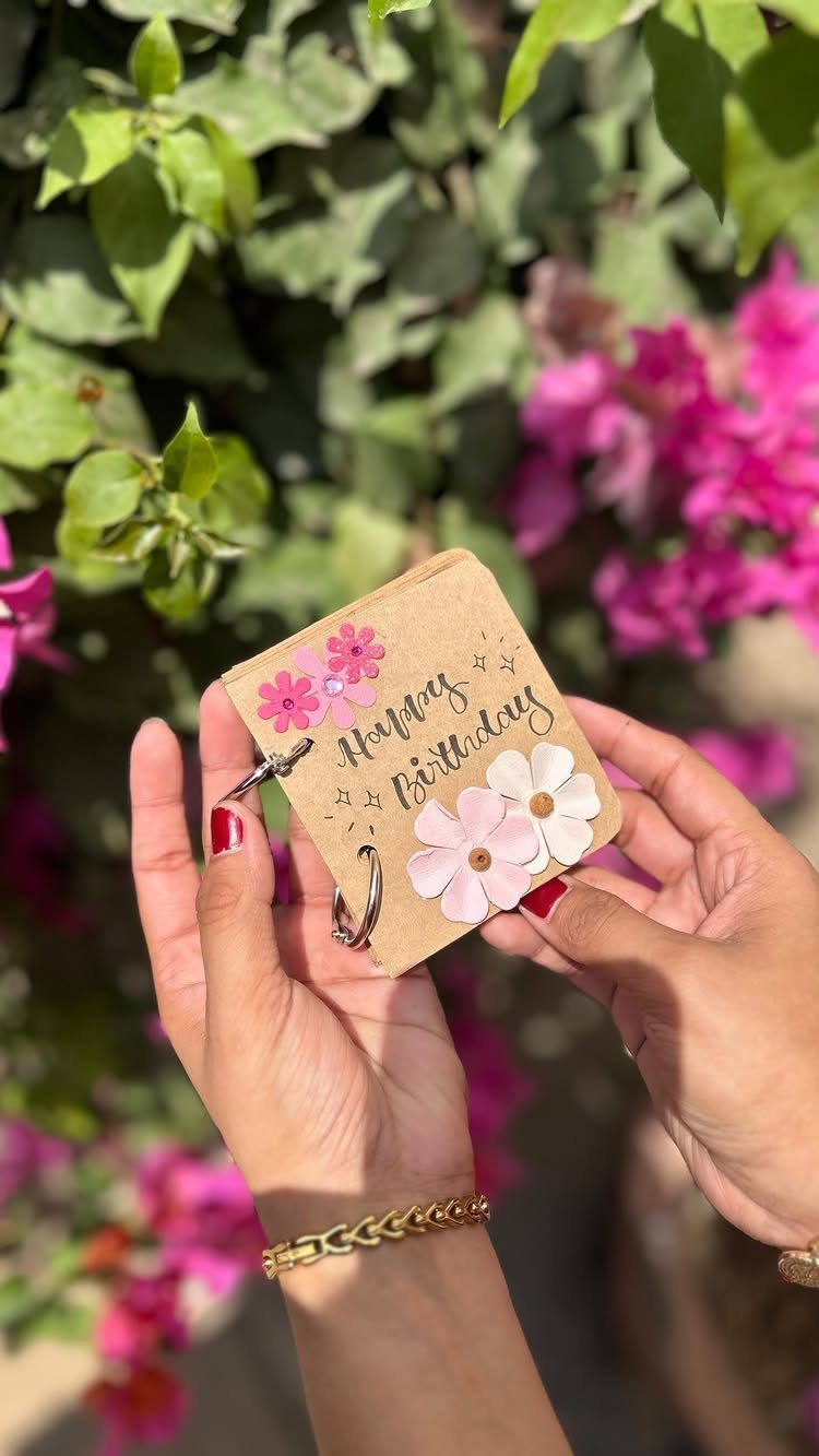Handmade birthday notebook with paper flowers held against a floral garden background.