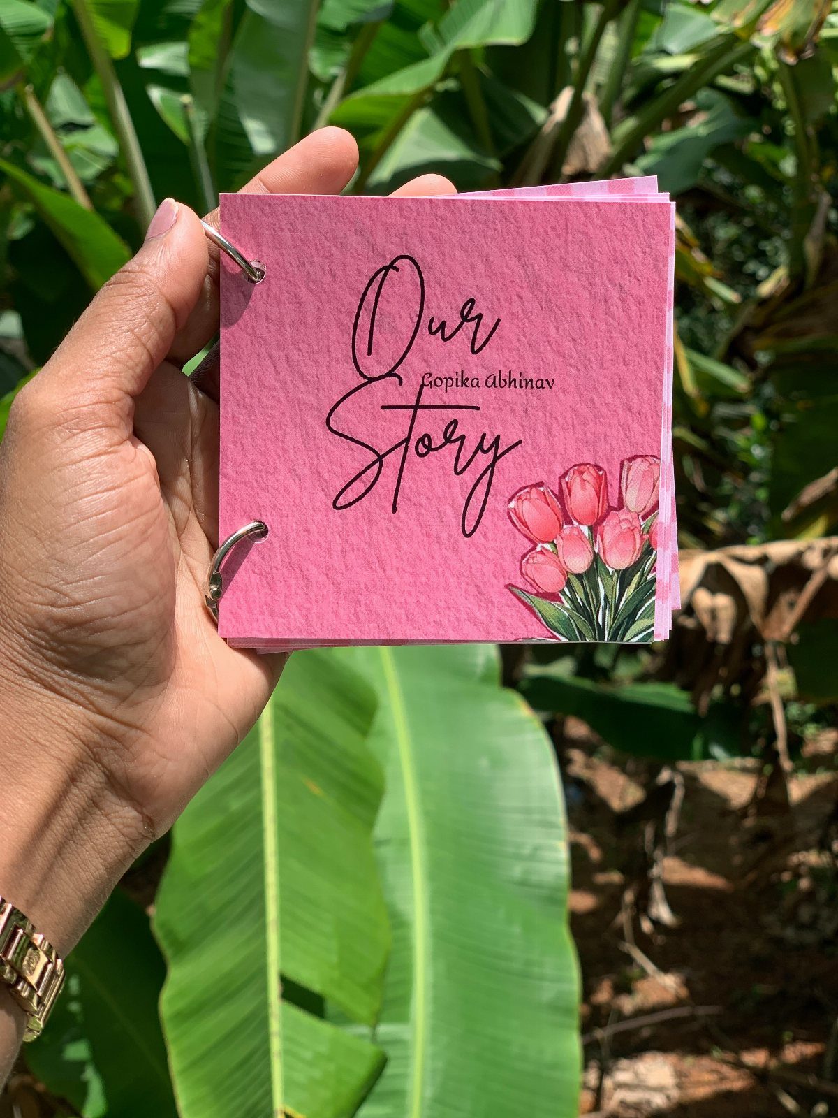 Hand holding a pink handmade book titled Our Story with tulip illustrations.