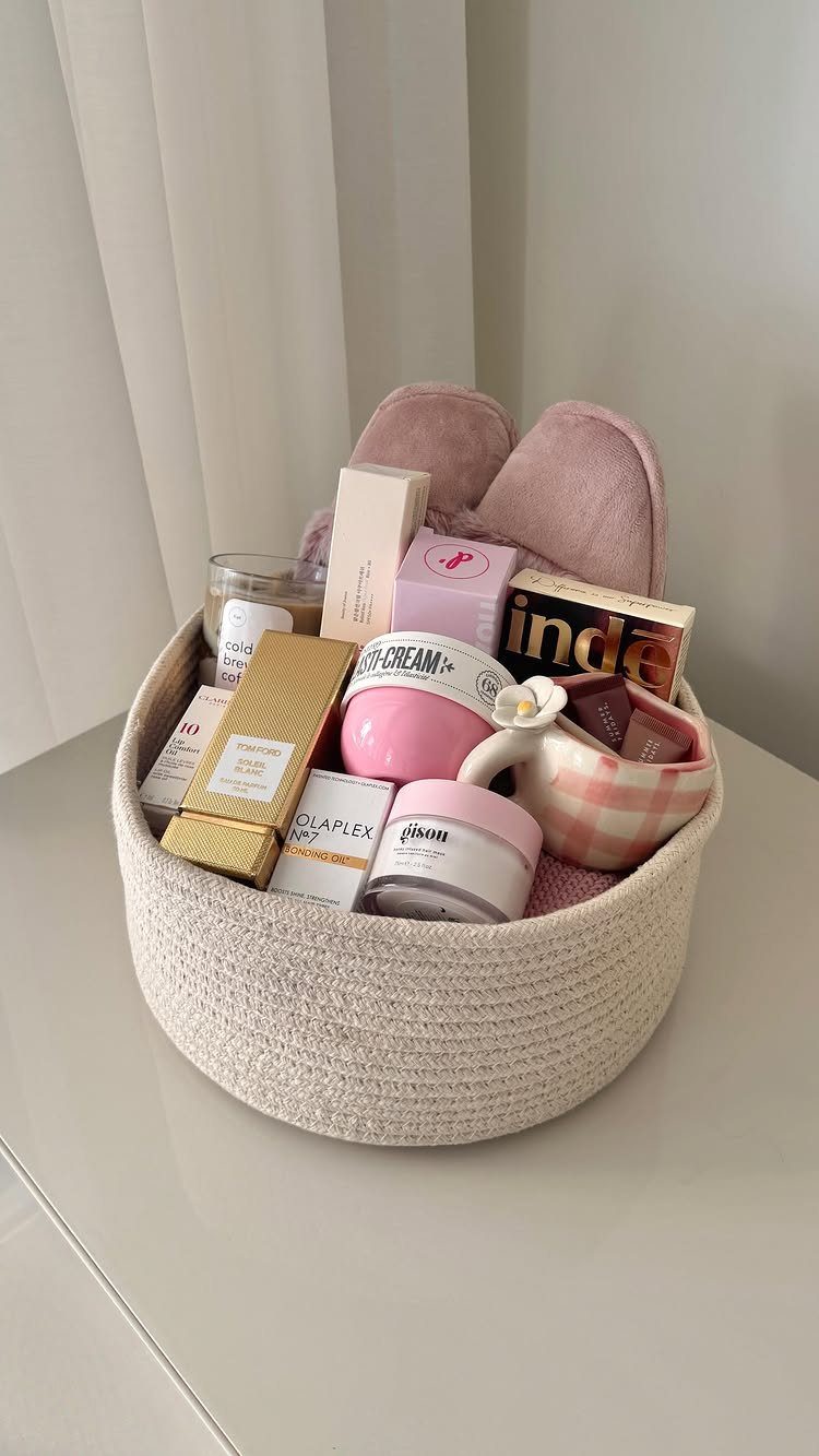 White woven gift basket filled with pink skincare products, candles, and fluffy slippers.