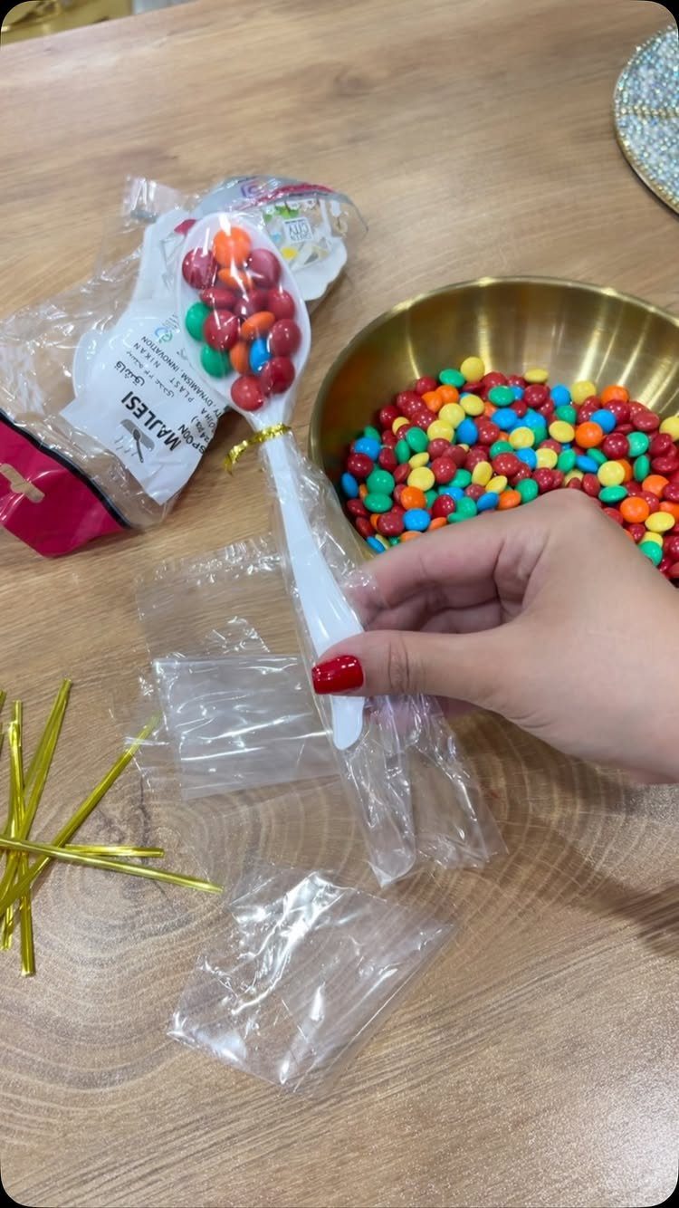 Hand holding a plastic spoon of colorful candy wrapped in clear plastic.