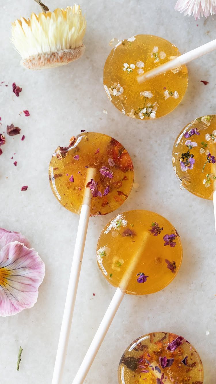 Amber lollipops with dried edible flowers on a light grey stone surface.