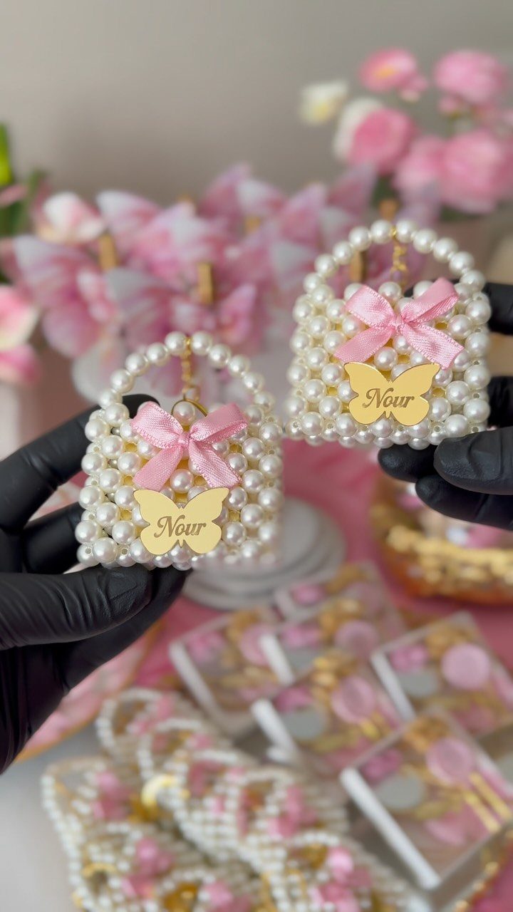 Two small pearl-beaded purses with pink bows and gold butterfly charms held by hands.