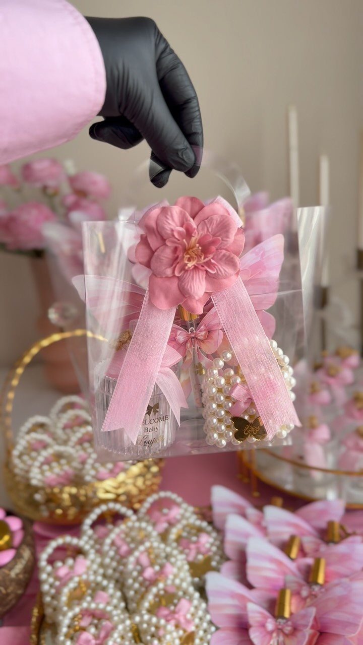 Clear gift bag with pink flower and pearl bracelet held by gloved hand.