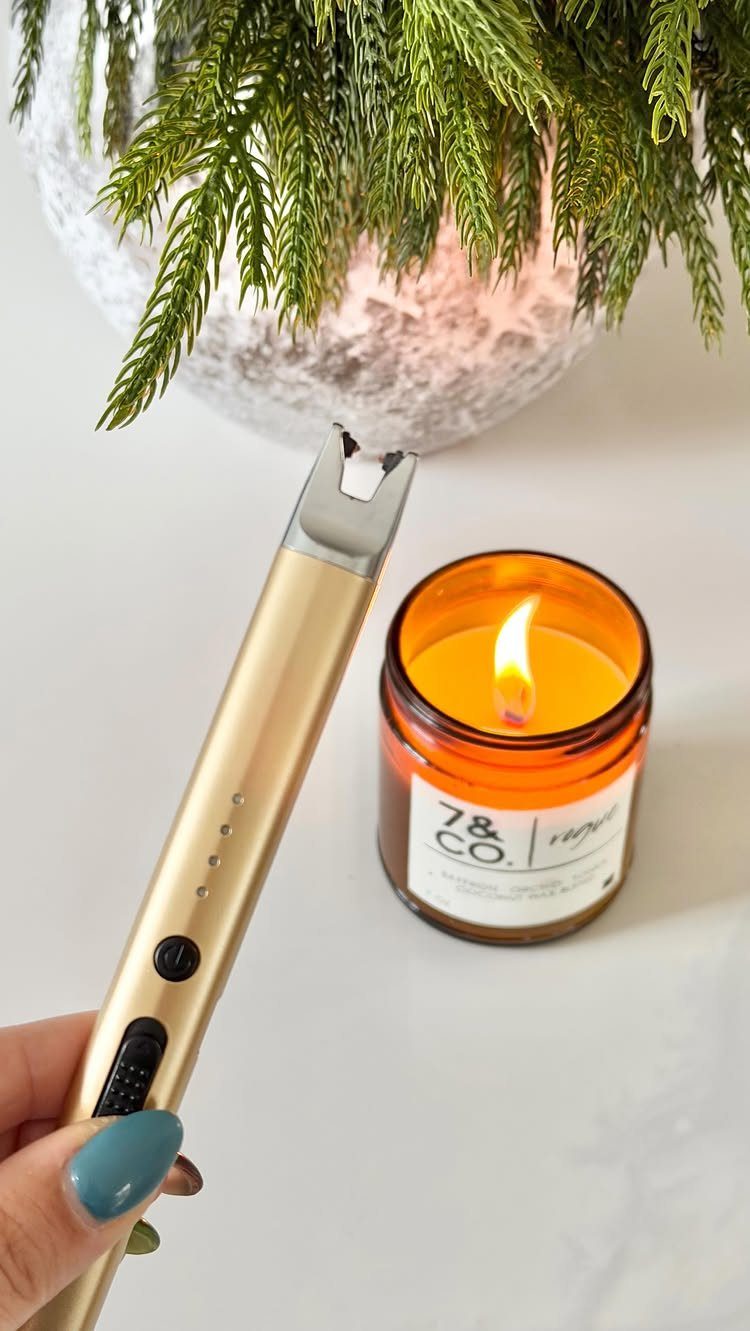 Gold electric candle lighter lighting a scented candle in an amber glass jar.