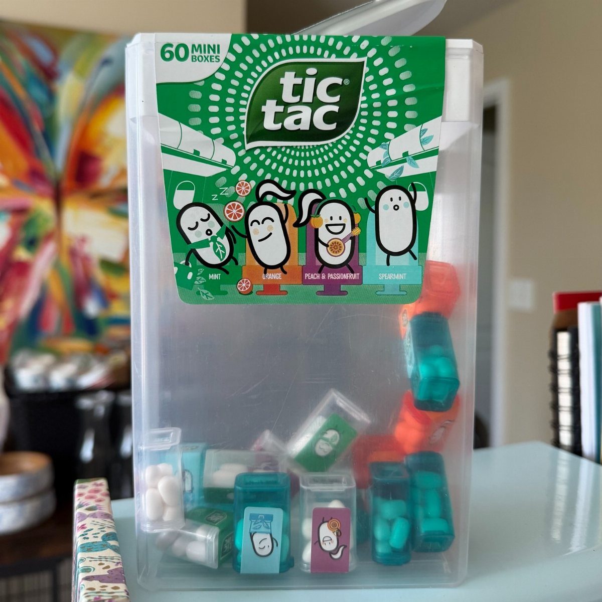 Giant clear plastic Tic Tac container filled with many small colorful mint boxes.
