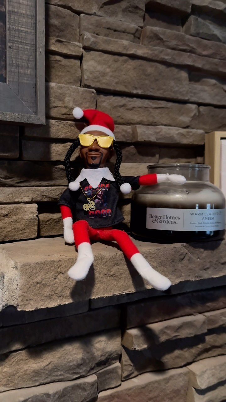 Snoop Dogg elf figurine wearing a Santa hat and yellow sunglasses on stone ledge